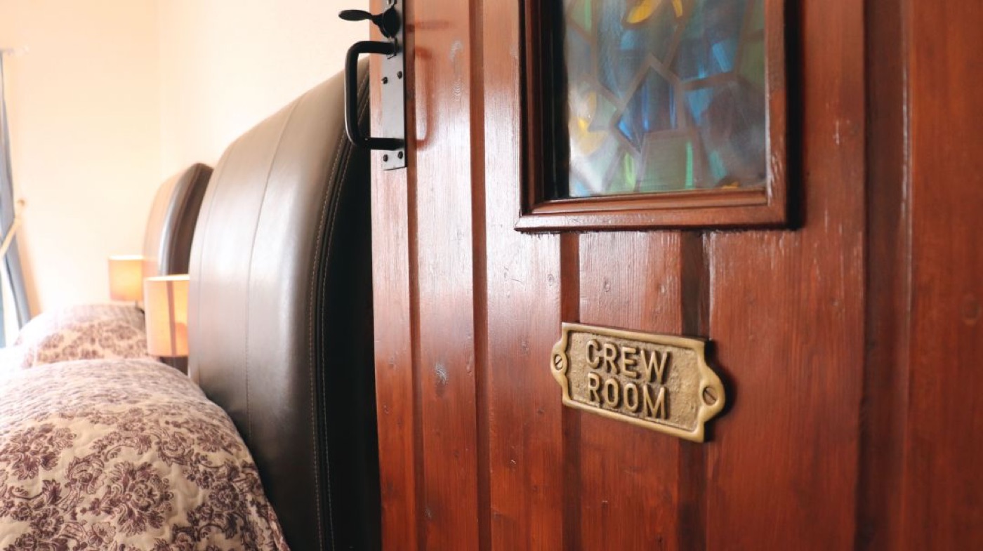 The brass Crew Room sign on the bedroom door, with the twin beds beyond